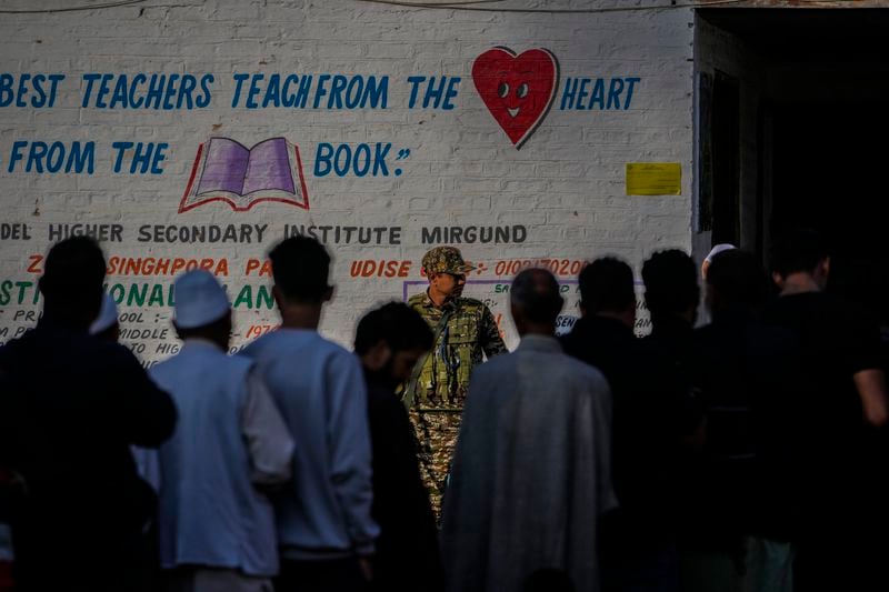 An Indian paramilitary soldier guards as Kashmiris queue up at a polling booth to cast their vote during the final phase of an election to choose a local government in Indian-controlled Kashmir, north of Srinagar, Tuesday, Oct.1, 2024. (AP Photo/Mukhtar Khan)