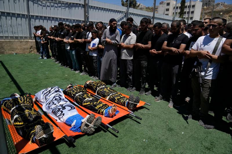 Mourners pray over the bodies of four Palestinians, wrapped with Islamic Jihad flags, who were killed by an Israeli airstrike late Tuesday, during their funeral in the West Bank refugee camp of Nur Shams, near Tulkarem, Wednesday, July 3, 2024. Palestinian health officials say four Palestinians were killed by an Israeli airstrike in a refugee camp in the northern West Bank late Tuesday. Israel's military said an aircraft struck a group of militants who were planting explosives in Nur Shams refugee camp near Tulkarem. (AP Photo/Nasser Nasser)