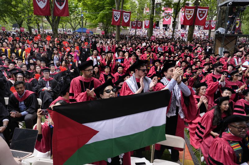 A student holds up the flag of Palestine as the 13 students, who have been barred from graduating due to protest activities, are recognized by a student address speaker during the commencement in Harvard Yard at Harvard University, Thursday, May 23, 2024, in Cambridge, Mass. (AP Photo/Charles Krupa)