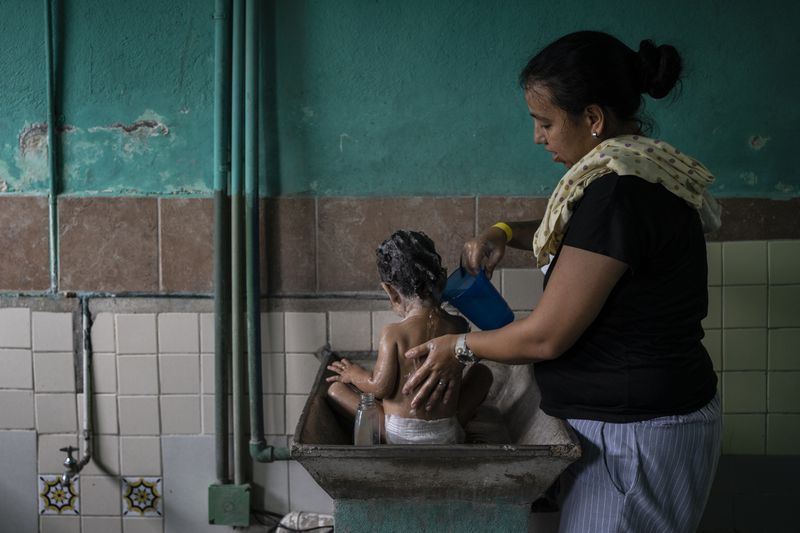 Rosana Mercado, a Venezuelan migrant, bathes her daughter inside the Peace Oasis of the Holy Spirit Amparito shelter, in Villahermosa, Mexico, Friday, June 7, 2024. After the head of Mexico's immigration agency ordered a halt to deportations in December, migrants have been left in limbo as authorities round up migrants across the country and dump them in the southern Mexican cities of Villahermosa and Tapachula. (AP Photo/Felix Marquez)