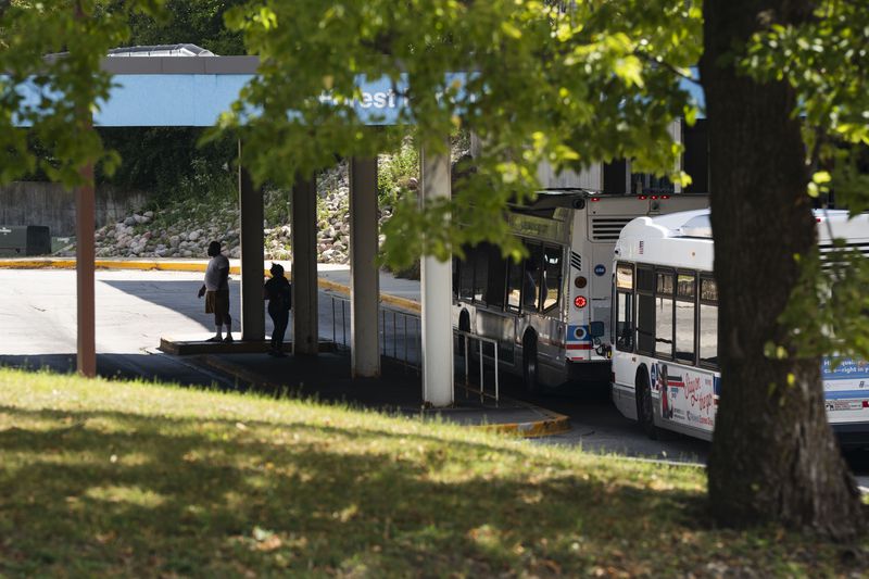 Commuters wait for a bus outside the Forest Park Blue Line train station in Forest Park, Ill., which remains closed, after four people were fatally shot on the train early Monday, Sept. 2, 2024. (Pat Nabong/Chicago Sun-Times via AP)