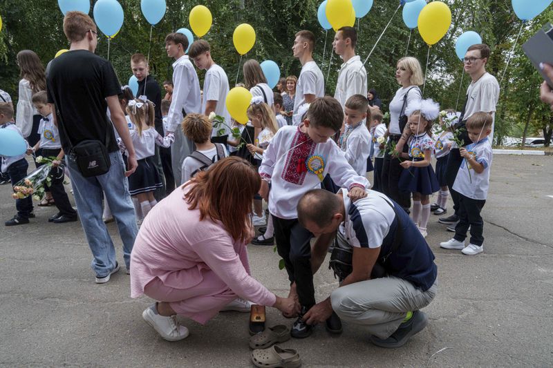 Parents help their son before the traditional ceremony for the first day of school in Zaporizhzhia, Ukraine, Sunday Sept. 1, 2024. Zaporizhzhia schoolchildren celebrated the traditional first day of school near the frontline. With the front just 40 kilometers away, the war is never far from the minds of teachers and families. (AP Photo/Evgeniy Maloletka)