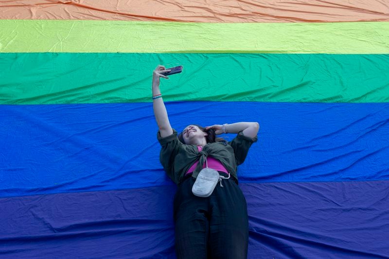 A woman takes a photo of herself while laying on the rainbow flag during a pride march in Belgrade, Serbia, Saturday, Sept. 7, 2024. (AP Photo/Marko Drobnjakovic)