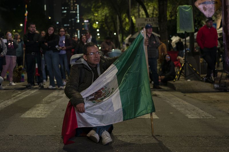 A man carrying a Mexican flag watches the senators' vote on a large screen during a protest against government's proposed judicial reform, which would make judges stand for election, outside the Senate in Mexico City, Tuesday, Sept. 10, 2024. (AP Photo/Felix Marquez)