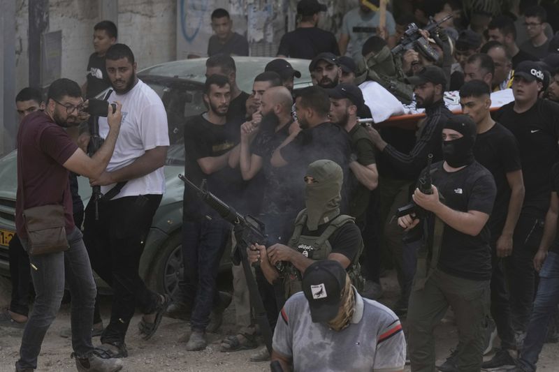 A masked gunman fires in the air during the funeral of Palestinian men who were killed in an Israeli military operation, in Jenin, West Bank, Friday, Sept. 6, 2024. (AP Photo/Majdi Mohammed)