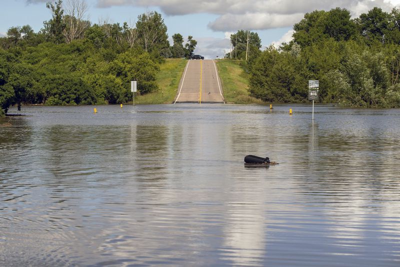 A South Dakota Highway Patrol Officer keeps watch over a flooded bridge that was underwater after days of heavy rain led to flooding in the area, near Lake Alvin, S.D., Saturday, June 22, 2024. (AP Photo/Josh Jurgens)