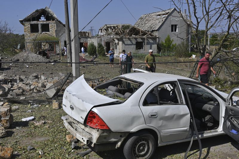 People walk in front of their damaged houses after Russian rocket attack in Usatove village near Odesa, Ukraine, Monday, Aug. 26, 2024. (AP Photo/Michael Shtekel)