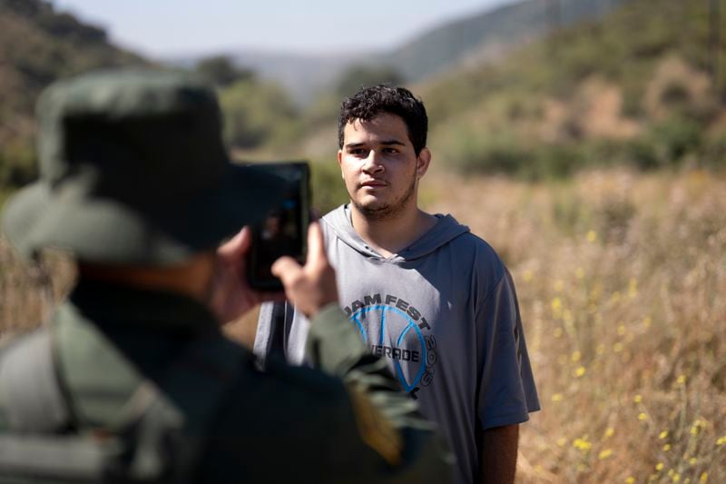 A migrant seeking asylum stands as a Border Patrol agent takes his picture before being transported and processed, Wednesday, June 5, 2024, near Dulzura, Calif. President Joe Biden on Tuesday unveiled plans to enact immediate significant restrictions on migrants seeking asylum at the U.S.-Mexico border as the White House tries to neutralize immigration as a political liability ahead of the November elections. (AP Photo/Gregory Bull)