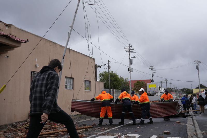 Rescue workers among damaged buildings in the Wynberg neighborhood of Cape Town, South Africa, Thursday, July 11, 2024. The area was hit overnight during strong winds that blew off roofs, destroyed parts of houses and other buildings, and brought down electricity poles. (AP Photo/Nardus Engelbrecht)