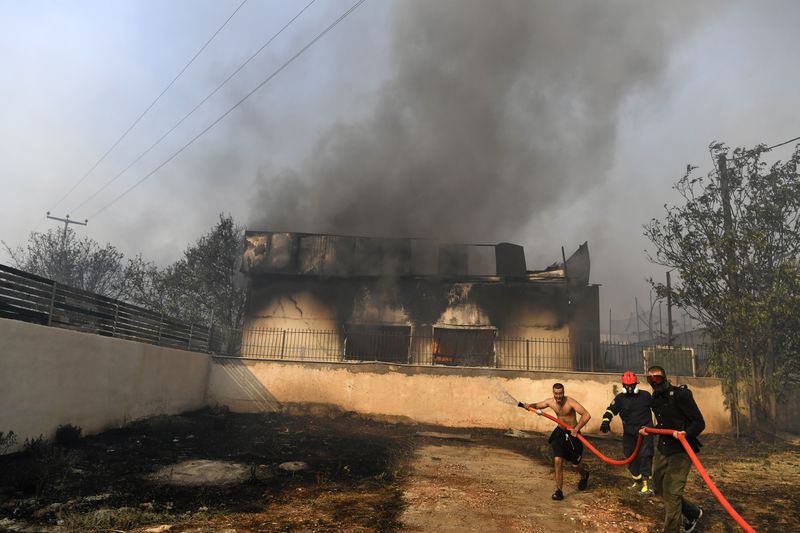 Two men and a volunteer firefighter try to extinguish the flames at a burning business during a fire in northern Athens, Monday, Aug. 12, 2024, as hundreds of firefighters tackle a major wildfire raging out of control on fringes of Greek capital. (AP Photo/Michael Varaklas)