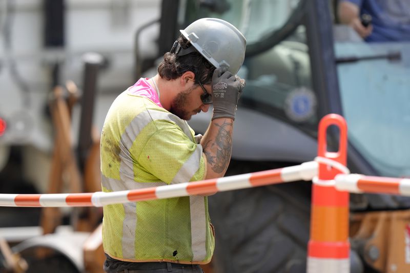 A worker adjusts his helmet while working in temperatures above 90 degrees at a gas line work site, Thursday, June 20, 2024, on a street, in Boston. (AP Photo/Steven Senne)