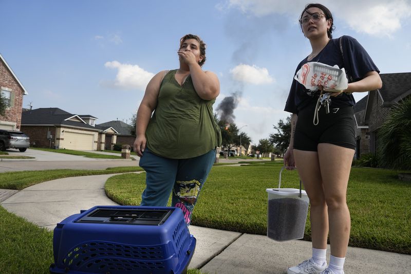 Meadow Way Drive residents Maddy Graham, right, and Ashley Cordova are self evacuating with cat, Mitzi, as the pipeline fire burns in the background Monday, Sept. 16, 2024, in Deer Park, Texas. (Yi-Chin Lee/Houston Chronicle via AP)