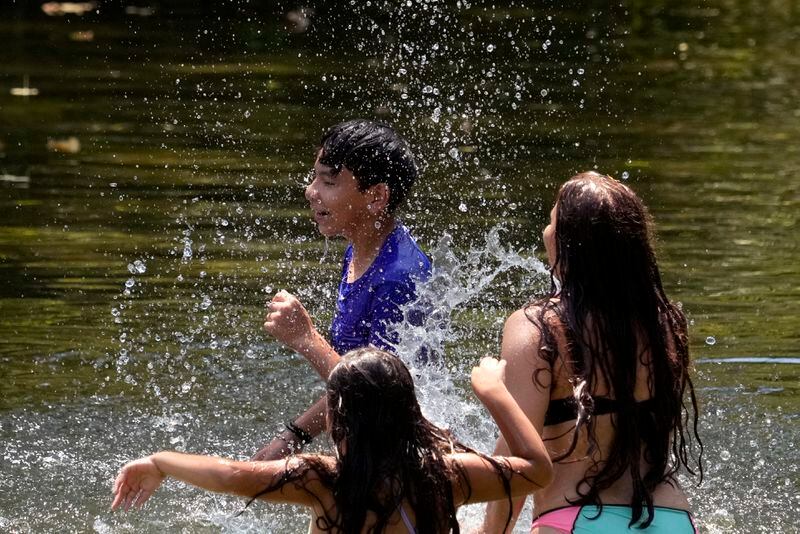 Romeo Gutierrez, center, is splashed by siblings Cipporah, left, and Leeann, right, as they keep cool in the Guadalupe River, Wednesday, Aug. 21, 2024, in New Braunfels, Texas. (AP Photo/Eric Gay)