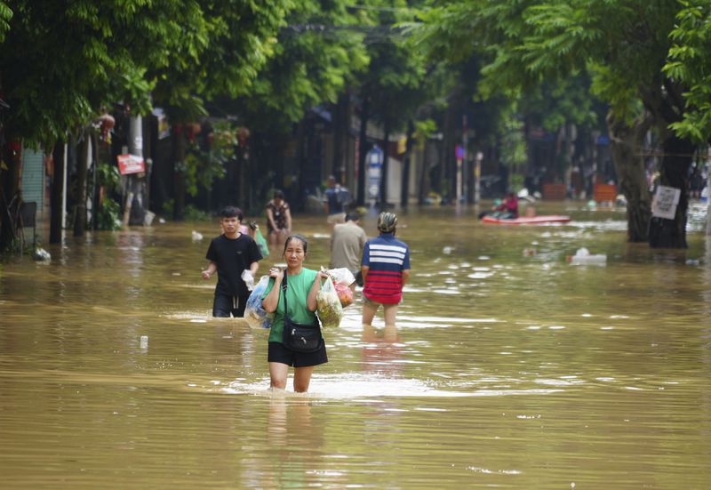 A woman carrying food wades in a flooded street in the aftermath of Typhoon Yagi, in Hanoi, Vietnam on Thursday, Sept. 12, 2024. (AP Photo/Hau Dinh)