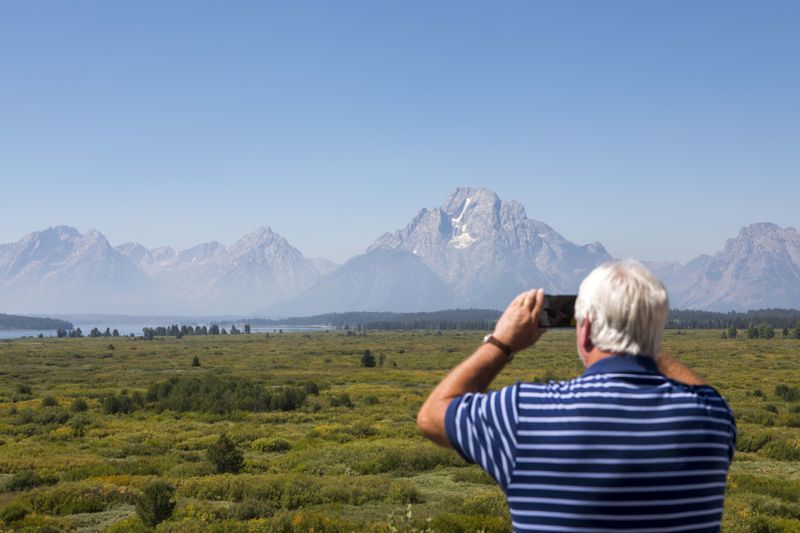 Steve Carringer of Tennessee takes a photo of the mountains at Jackson Lake Lodge, the site of the Jackson Hole Economic Symposium, in Grand Teton National Park near Moran, Wyo., on Thursday, Aug. 22, 2024. (AP Photo/Amber Baesler)