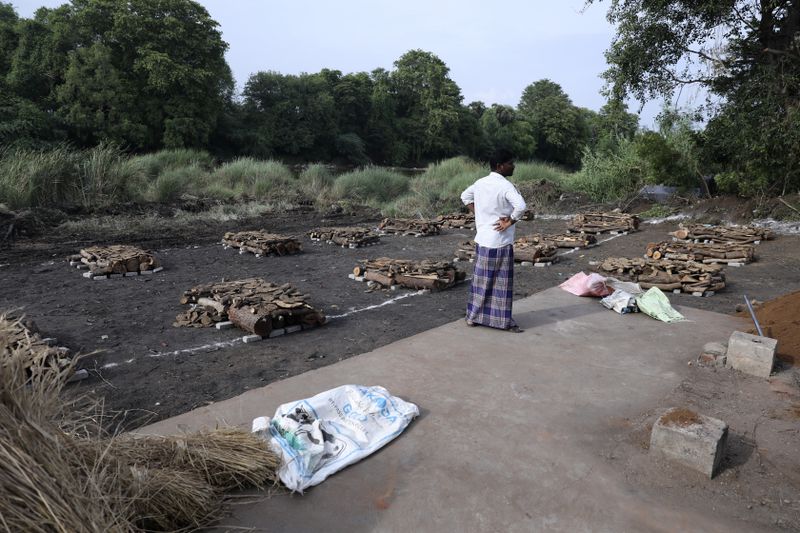 A man stands next to piles of wood arranged for the mass cremation of people, who died after drinking illegally brewed liquor, in Kallakurichi district of the southern Indian state of Tamil Nadu, India, Thursday, June 20, 2024. The state's chief minister M K Stalin said the 34 died after consuming liquor that was tainted with methanol, according to the Press Trust of India news agency. (AP Photo/R. Parthibhan)