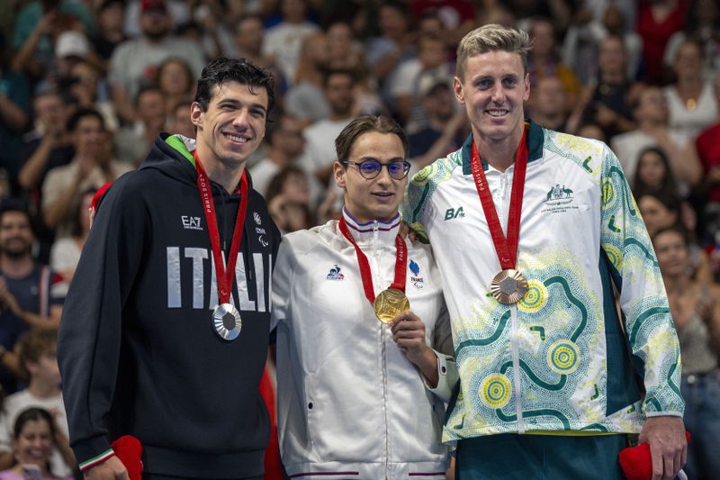 Paralympic athlete Ugo Didier, of France, centre, Simone Barlaam, of Italy, left, and Breden Hall, of Australia, celebrate at the podium after the Men's 400 Freestyle -S9, during the 2024 Paralympics, Thursday, Aug. 29, 2024, in Paris, France. (AP Photo/Emilio Morenatti)