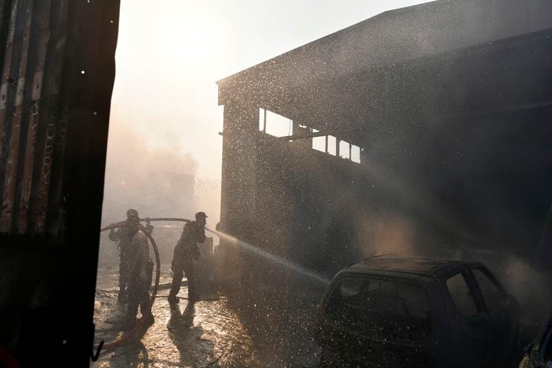 Two men and a volunteer firefighter try to extinguish the flames at a burning business during a fire in northern Athens, Monday, Aug. 12, 2024, as hundreds of firefighters tackle a major wildfire raging out of control on fringes of Greek capital. (AP Photo/Michael Varaklas)