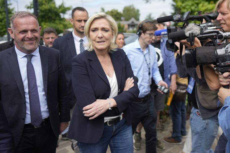 French far right leader Marine Le Pen, center, with local mayor Steeve Briois, left, leave after voting in the first round of the parliamentary election, Sunday, June 30, 2024 in Henin-Beaumont, northern France. France is holding the first round of an early parliamentary election that could bring the country's first far-right government since Nazi occupation during World War II. The second round is on July 7, and the outcome of the vote remains highly uncertain. (AP Photo/Thibault Camus)