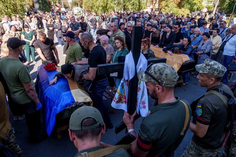 Relatives and friends mourn over the coffins of six Ukrainian servicemen killed in a Russian rocket attack at a Ukrainian military academy, during their funeral ceremony in Poltava, Ukraine, Saturday Sept. 7, 2024. (AP Photo/Evgeniy Maloletka)