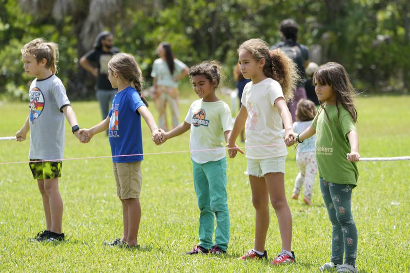 Children hold hands as they use yarn to outline the area a pickleball court would occupy, during a protest against Gov. Ron DeSantis' plan to develop state parks with business ventures such as golf courses, pickleball courts and large hotels, during a demonstration at Oleta River State Park, Tuesday, Aug. 27, 2024, in North Miami Beach, Fla. (AP Photo/Wilfredo Lee)