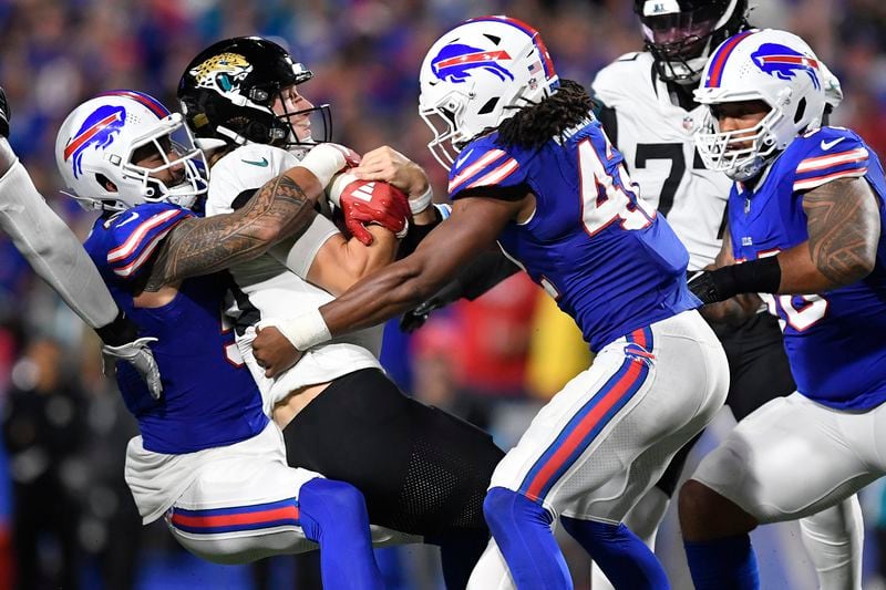 Jacksonville Jaguars quarterback Trevor Lawrence, center, is sacked by Buffalo Bills defensive end AJ Epenesa, left, and linebacker Dorian Williams (42) during the second half of an NFL football game Monday, Sept. 23, 2024, in Orchard Park, NY. (AP Photo/Adrian Kraus)