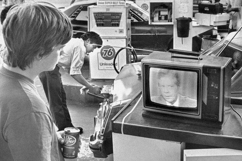 FILE - College student Chuck McManis watches President Jimmy Carter's nationally televised energy speech from a service station in Los Angeles, as a gas station attendant fills up a customer's car, July 15, 1979. (AP Photo/Mao, File)