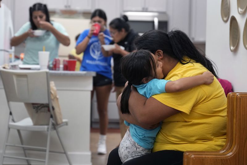 Alexandra Reynoso, right, hugs her little sister, Sofia Reynosa, 5, as others grab a bite to eat in the kitchen of St. Michael the Archangel Catholic church in the aftermath of Hurricane Helene Friday, Oct. 4, 2024, in Erwin, Tenn. (AP Photo/Jeff Roberson)