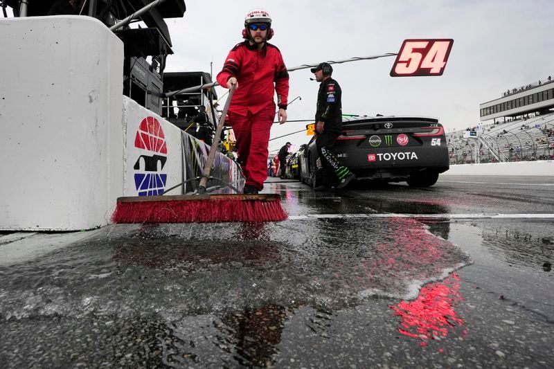 A member of the New Hampshire Motor Speedway pit lane fire crew uses a broom to remove water during a rain delay in a NASCAR Cup Series race, Sunday, June 23, 2024, at the race track in Loudon, N.H. (AP Photo/Steven Senne)