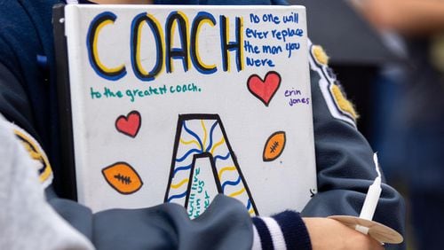 A mourner holds a sign honoring Apalachee High School football assistant coach Richard "Ricky" Aspinwall at a vigil at Jug Tavern Park on Sept. 6, 2024, in Winder, Georgia. A 14-year-old Apalachee High School student is accused of shooting and killing two fellow students, Aspinwall and another teacher and injuring nine others at the Barrow County high school on Wednesday. (Arvin Temkar/The Atlanta Journal-Constitution/TNS)