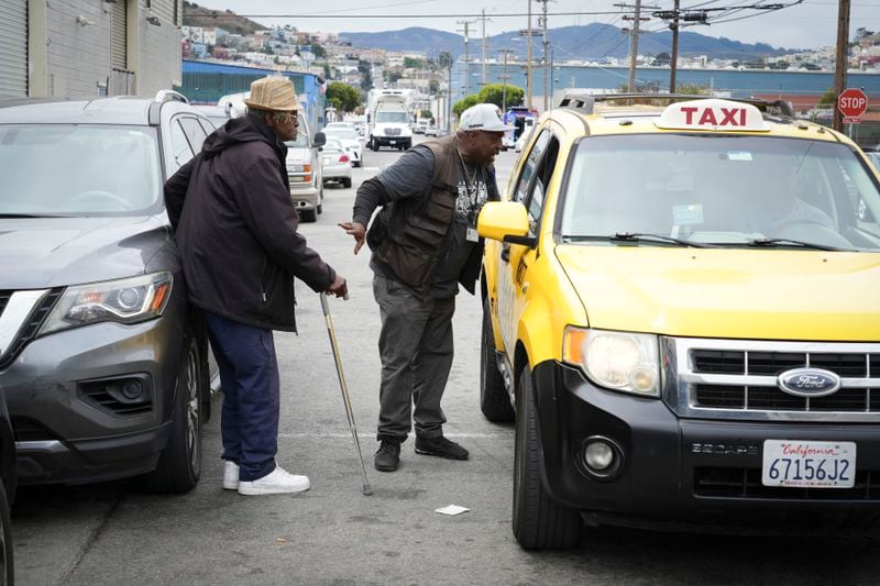 Ventrell Johnson, middle, of the San Francisco Homeless Outreach Team, helps call a taxi for Larry James Bell, a homeless resident who will be moving from temporary shelter into permanent housing Tuesday, Sept. 10, 2024, in San Francisco. (AP Photo/Terry Chea)