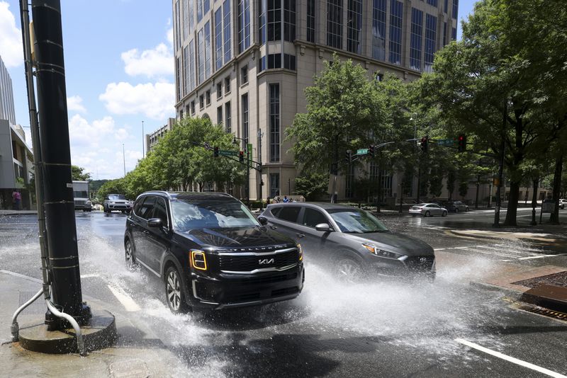 Automobiles travel on 14th street as they drive through water spilled from a fire hydrant on West Peachtree Street, Monday, June 3, 2024, in Atlanta. (Jason Getz / AJC)
