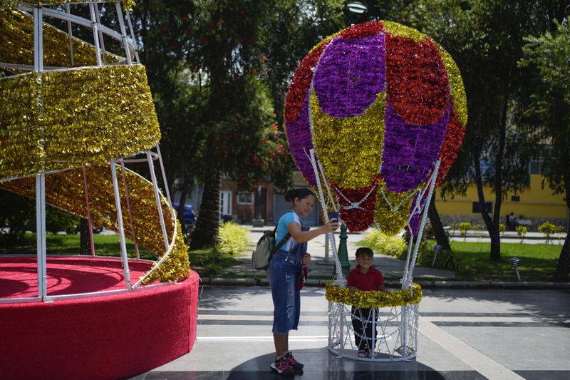 A woman takes a selfie with her daughter inside a Christmas decoration in Caracas, Venezuela, Tuesday, Oct. 1, 2024. (AP Photo/Ariana Cubillos)