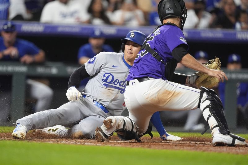 Los Angeles Dodgers' Shohei Ohtani, left, slides safely into home plate to score on a double hit by Kevin Kiermaier as Colorado Rockies catcher Jacob Stallings turns to apply a late tag in the eighth inning of a baseball game Friday, Sept. 27, 2024, in Denver. (AP Photo/David Zalubowski)