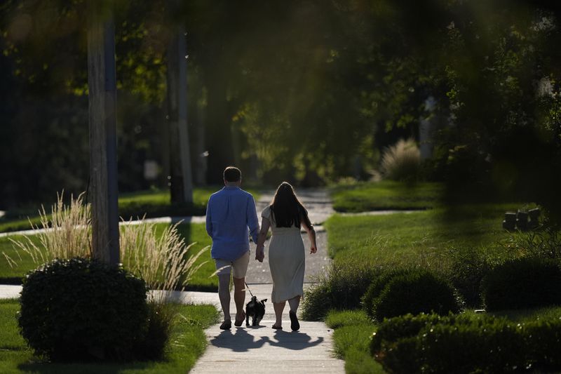 Steve and Julia Manetta take their dog Basil for a walk after dinner Thursday, Aug. 29, 2024, in Lemont, Ill. (AP Photo/Charles Rex Arbogast)