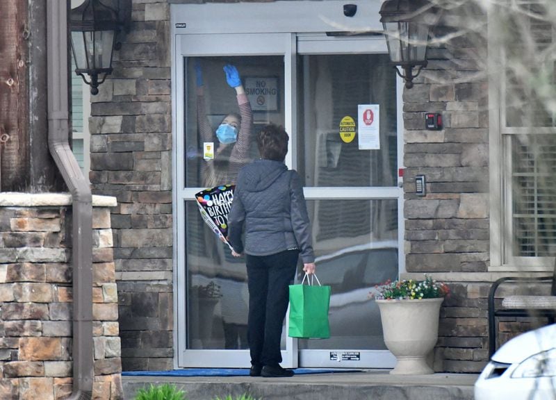 A worker unlocks the door at The Retreat at Canton as a visitor holds a birthday ballon at the front entrance. A family delivered the ballon and a gift bag to a relative at the assisted living community but could not go in after an outbreak of coronavirus there. Three residents and one employee have “tested presumptively positive” for COVID-19. (Hyosub Shin / Hyosub.Shin@ajc.com)