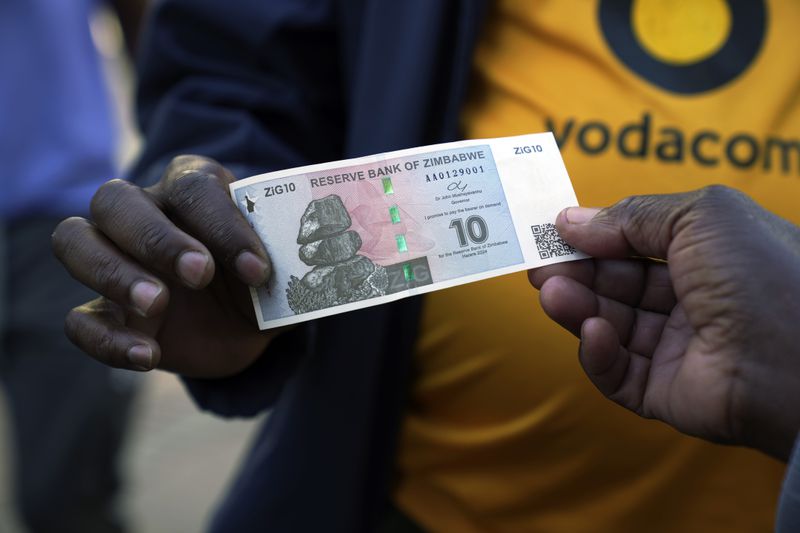 Street vendors hold the new currency note called the ZiG, in Harare, Zimbabwe, Tuesday, April 30, 2024. Authorities in Zimbabwe are resorting to force to defend the new currency, including packing jail cells with dozens of street currency dealers and freezing accounts of hordes of businesses accused of undermining the value of the ZiG. (AP Photo/Tsvangirayi Mukwazhi)
