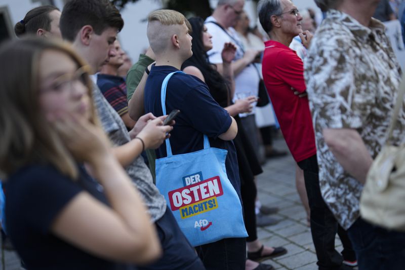 A young man with a bag reading "The east does it" attends an election campaign rally of the far-right Alternative for Germany, AfD, party in Suhl, Germany, Tuesday, Aug. 13, 2024. (AP Photo/Markus Schreiber)