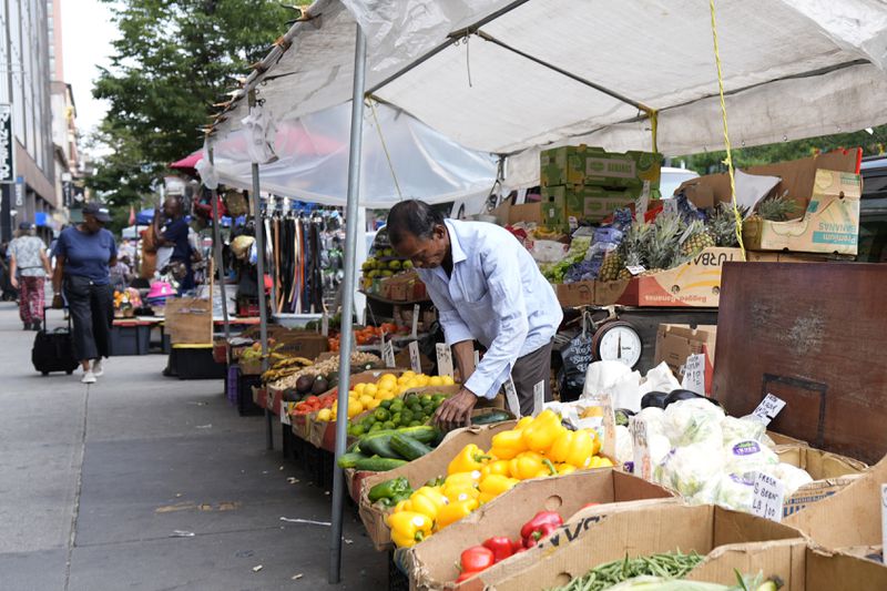 A man adjusts a street grocery display in the Harlem neighborhood of New York, Thursday, Aug. 15, 2024. (AP Photo/Pamela Smith)