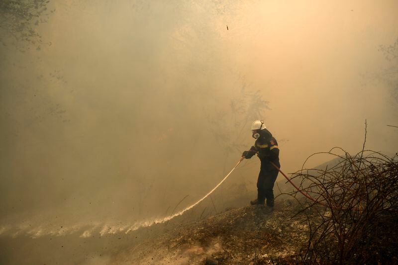 A firefighter tries to extinguish a fire in northern Athens, Monday, Aug. 12, 2024, as hundreds of firefighters tackle a major wildfire raging out of control on fringes of Greek capital. (AP Photo/Michael Varaklas)