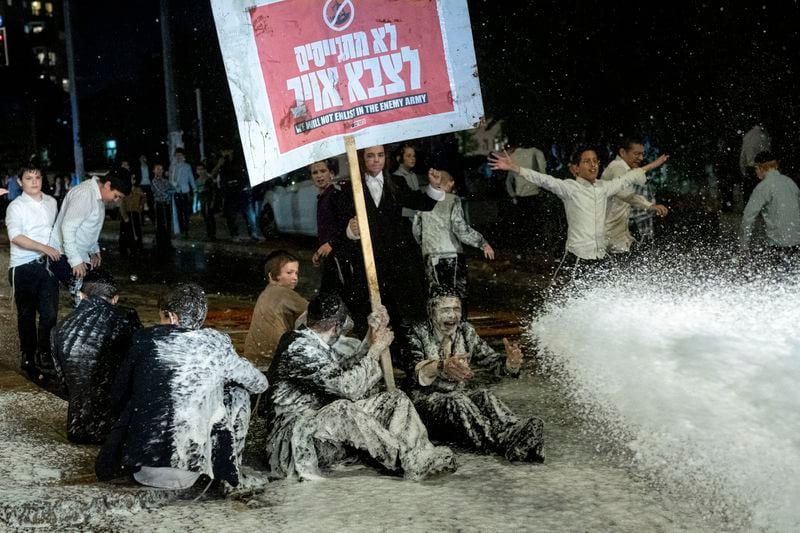 Police use a water cannon to disperse ultra-Orthodox Jewish men blocking a street during a protest against army recruitment in Jerusalem, Sunday, June 30, 2024. Israel's Supreme Court last week ordered the government to begin drafting ultra-Orthodox men into the army, a landmark ruling seeking to end a system that has allowed them to avoid enlistment into compulsory military service. (AP Photo/Ohad Zwigenberg)