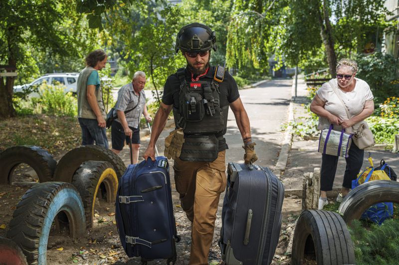 A volunteer on East SOS helps to carry bags of evacuees in Selidove, Donetsk region, Ukraine, Monday, August 19, 2024. Due to the advance of Russian troops, the war affects more and more new settlements to the west of the Donetsk region. Intensive shelling forced people to leave homes. (AP Photo/Evgeniy Maloletka)