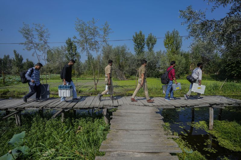 Polling officials and police walk on a wooden bridge towards a polling station in the interior of Dal Lake ahead of the second phase of voting for choosing a local government in Indian-controlled Kashmir, in Srinagar, Tuesday, Sept. 24, 2024. (AP Photo/Mukhtar Khan)