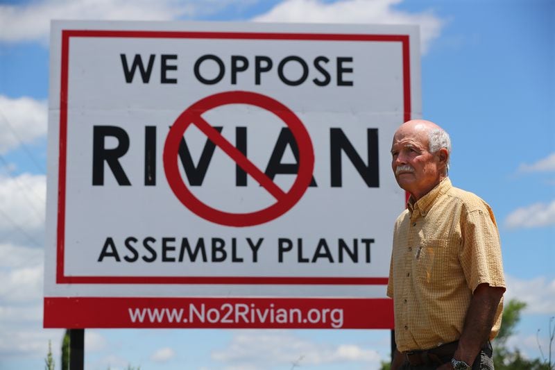 Rivian opponent George West stands near a large sign posted in a field on Davis Academy Road across the street from the planned $5 billion Rivian electric vehicle plant while showing the proposed location on Thursday, May 12, 2022, in Rutledge. “Curtis Compton / Curtis.Compton@ajc.com”