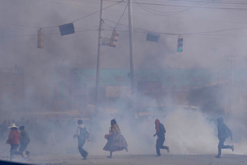 People run through tear gas thrown by police during clashes between supporters of former President Evo Morales and current President Luis Arce in El Alto, Bolivia, Sunday, Sept. 22, 2024. (AP Photo/Juan Karita)