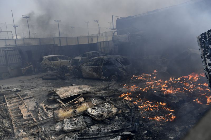 Flames burn next to damaged cars at a business during a fire in northern Athens, Monday, Aug. 12, 2024, as hundreds of firefighters tackle a major wildfire raging out of control on fringes of Greek capital. (AP Photo/Michael Varaklas)