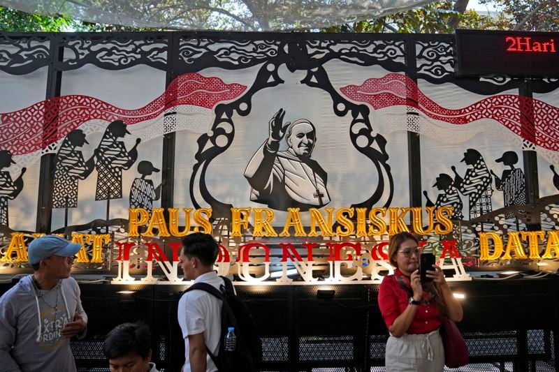 People walk past a welcoming signboard for Pope Francis displayed at Jakarta Cathedral in Jakarta, Indonesia, Sunday, Sept. 1, 2024, ahead of his visit to Indonesia from Sept. 3-6. (AP Photo/Dita Alangkara)