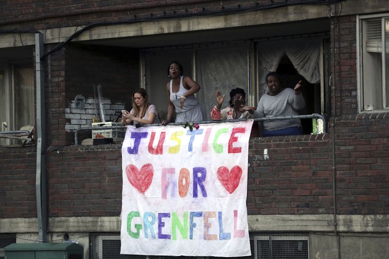 People watch from a balcony as people walk during a demonstration following the fire at Grenfell Towers that engulfed the 24-storey building on Wednesday morning, in London, Friday June 16, 2017. (AP Photo/Tim Ireland, File)