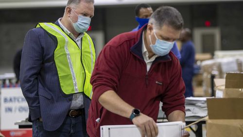 An elections observer (left) watches as Fulton County elections workers prepare absentee ballots for counting during the county's second recount of presidential election ballots on Nov. 25, 2020, at the Georgia World Congress Center. (Alyssa Pointer/The Atlanta Journal-Constitution)