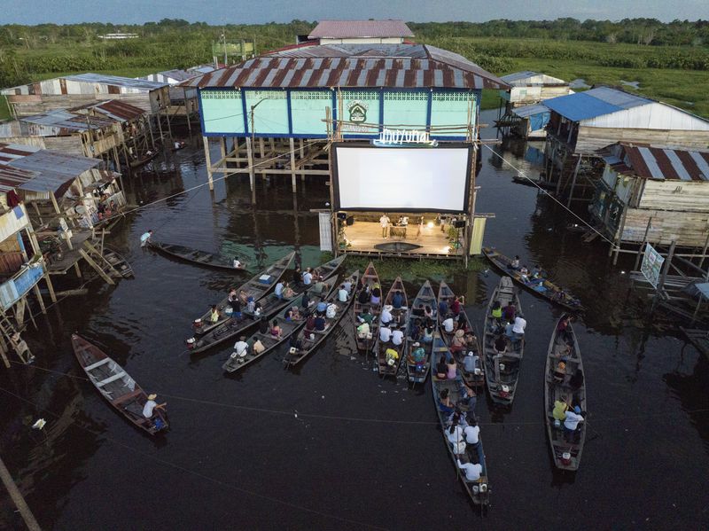Spectators watch a film projected on a screen set up on a wooden structure, from boats, during the Muyuna Floating Film Festival in the Belen neighborhood of Iquitos. The festival celebrates tropical forests, in the Belen neighborhood of Iquitos, Peru, Saturday, May 25, 2024. (AP Photo/Rodrigo Abd)